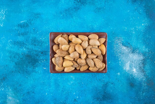 Shelled almonds in a plate on the blue surface