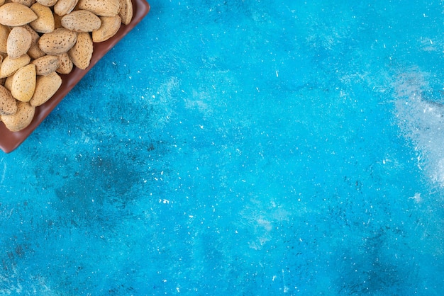 Shelled almonds in a plate on the blue surface