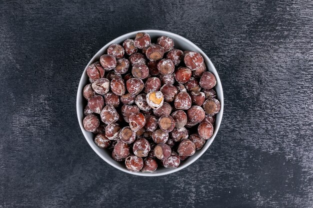 Shelled hazelnuts in a white bowl top view on a dark stone table