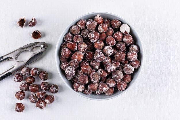 Shelled hazelnuts in a white bowl with nutcracker top view