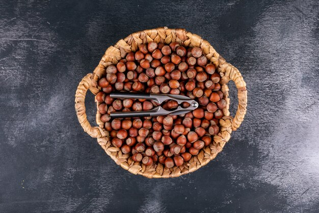 Shelled hazelnuts in a wicker basket with nutcracker top view on a dark stone table