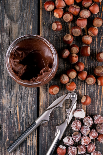 Shelled hazelnuts with cocoa spread and nutcracker top view on a dark wooden table