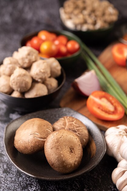 검은 시멘트 바닥에 마늘, 토마토, 고추, 파, 적 양파를 얹은 표고 버섯.