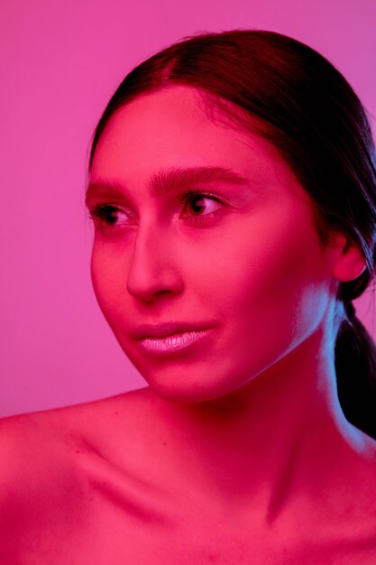 Shine. Beautiful east woman's portrait isolated on pink studio background in neon, monochrome. Female brunette model. Concept of human emotions, facial expression, sales, ad, fashion and beauty.