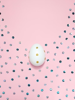 파스텔 핑크 배경에 황금색 원과 스팽글이 있는 흰색 달걀의 빛나는 수직 구성. 부활절 휴가를 위한 광고 콘텐츠. 평평한 평지, 위쪽 보기, 텍스트 복사 공간.