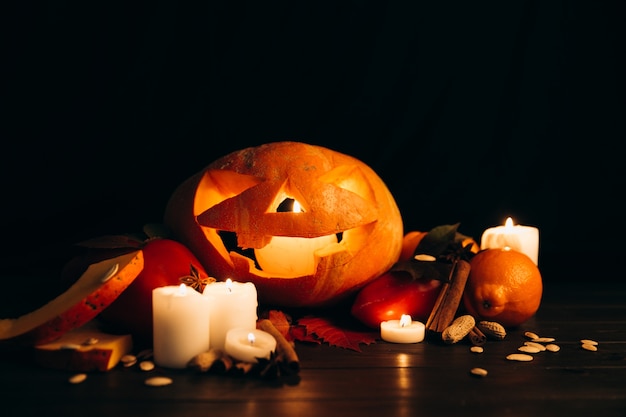 Shiny candles, cinnamon and fallen leaves stand before scarry halloween pumpkin Free Photo