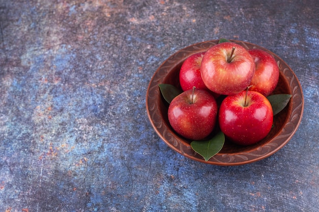 Shiny red apples with green leaves on stone background. 