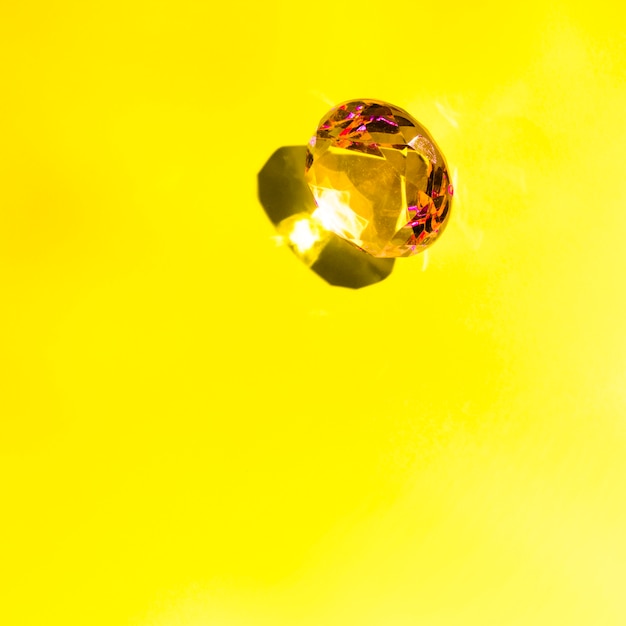 Shiny sparkling diamond with shadow on yellow background