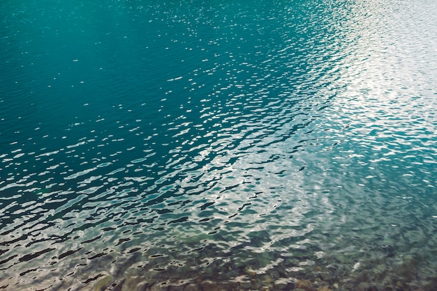 산 호수의 빛나는 질감 푸른 표면입니다. 투명한 물에 돌 바닥. 화창한 날에 맑은 물에 산의 반사와 미니 멀. copyspace와 수 중 돌입니다.
