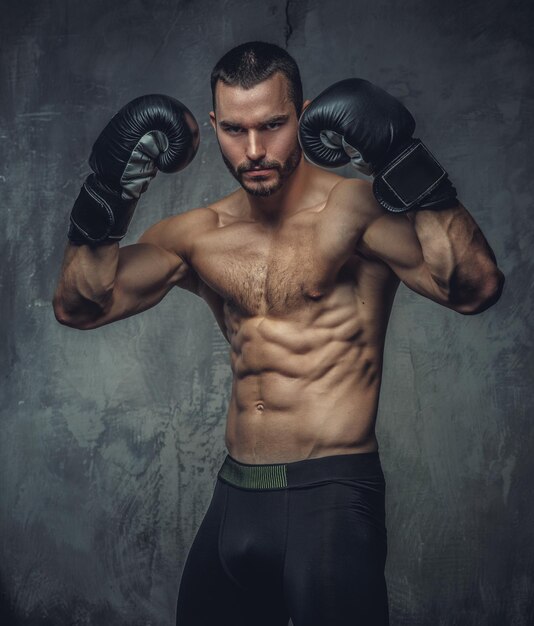 Shirtless aggressive fighter with burning boxer gloves on grey background.