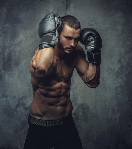 Агрессивный боец без рубашки с горящими боксерскими перчатками на сером фоне.