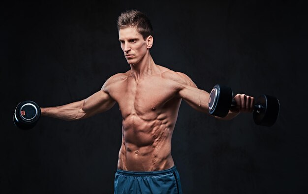 Shirtless athletic male doing shoulders lateral head exercises with dumbbells.