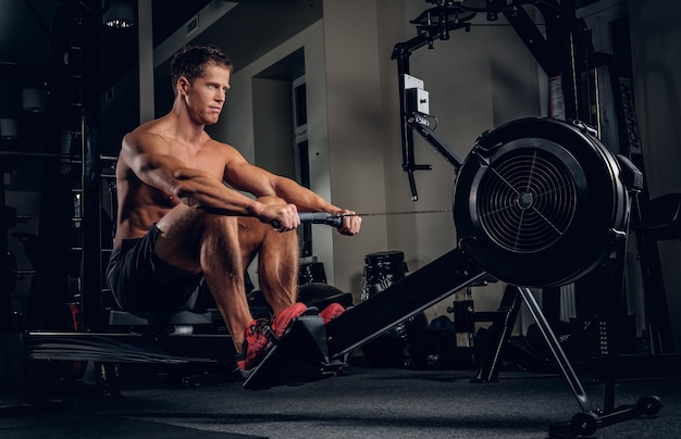 Бесплатное фото Спортивный мужчина без рубашки тренирует мышцы спины на силовой машине в тренажерном зале.