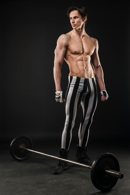 Free photo shirtless athletic man posing with weight set