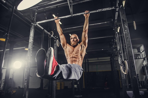 Shirtless bearded man doing stomach exercises on a horizontal bar.