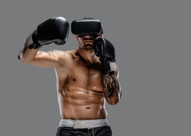 Shirtless brutal boxing fighter in virtual reality glasses on his head. Isolated on a grey background.