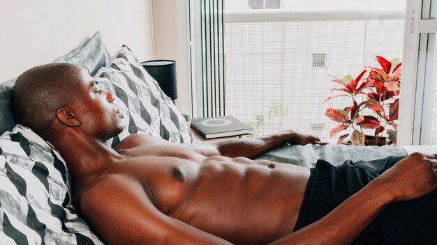 Shirtless fit african young man relaxing on bed