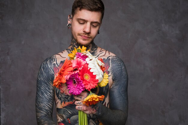 Shirtless hipster young man with tattoo on his body holding gerbera flowers in hand