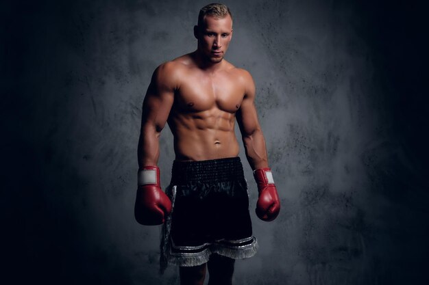 Shirtless kick boxer showing his punches and kicks over grey background in a studio.