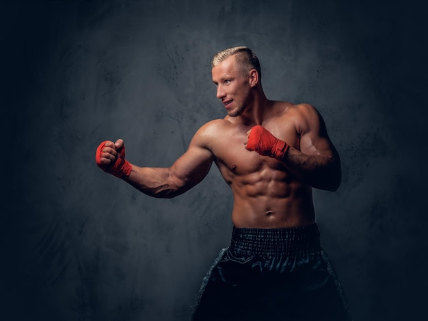 Shirtless kick boxer showing his punches and kicks over grey background in a studio.