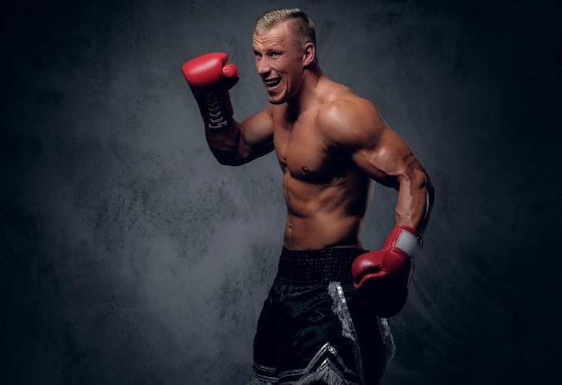 Shirtless kick boxer showing his punches and kicks over grey background in a studio.