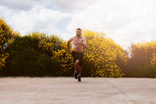 Shirtless male athlete running in front of flowering plants