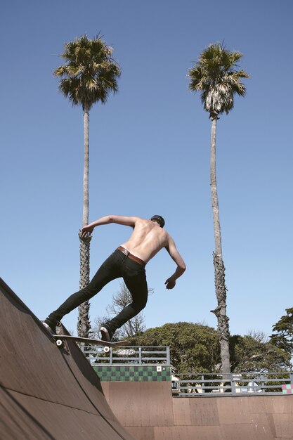 Мужчина без рубашки катается на скейтборде, делая трюк на открытом воздухе в дневное время