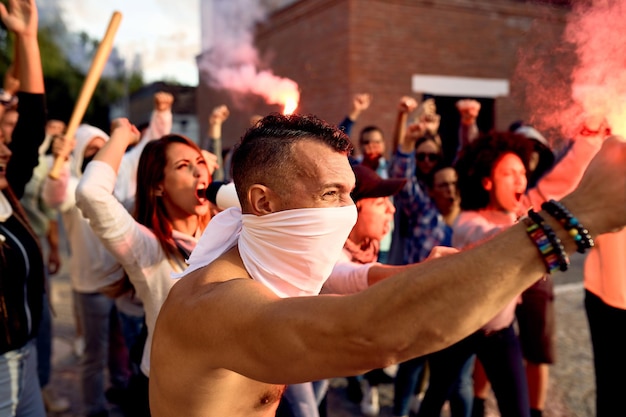 Uomo a torso nudo con in mano torce accese mentre protestava con una folla di persone durante manifestazioni pubbliche