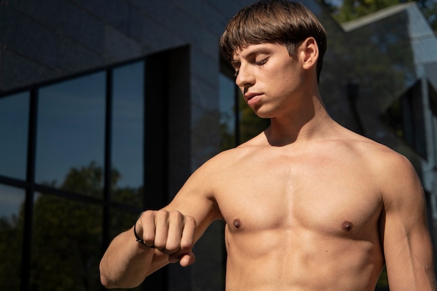 Foto gratuita uomo senza camicia guardando la sua fascia di fitness mentre si lavora fuori all'aperto