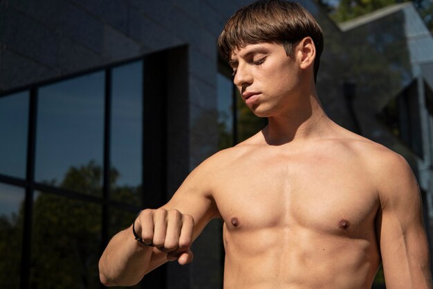 Shirtless man looking at his fitness band while working out outdoors