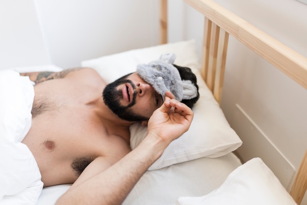 Foto gratuita uomo senza camicia che si trova sul letto sbirciando da una maschera per gli occhi