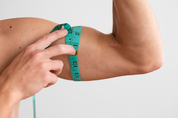 Shirtless man measuring his bicep with tape