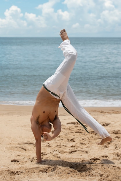 Free photo shirtless man practicing capoeira on the beach