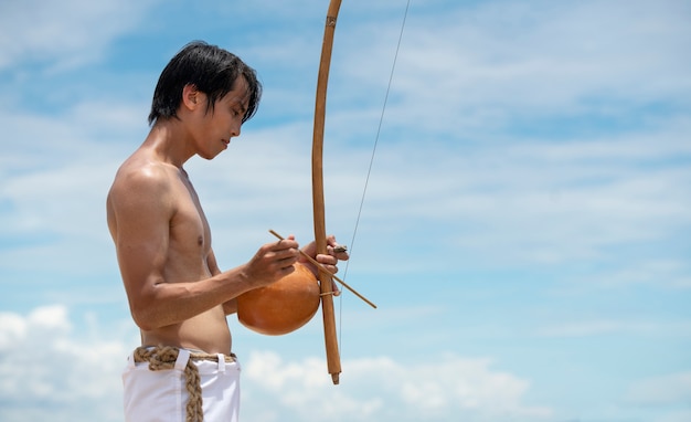 Uomo senza camicia che pratica capoeira sulla spiaggia con fiocco di legno