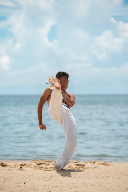 Uomo senza camicia che pratica capoeira da solo sulla spiaggia