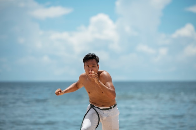 Foto gratuita uomo senza camicia che pratica capoeira da solo sulla spiaggia