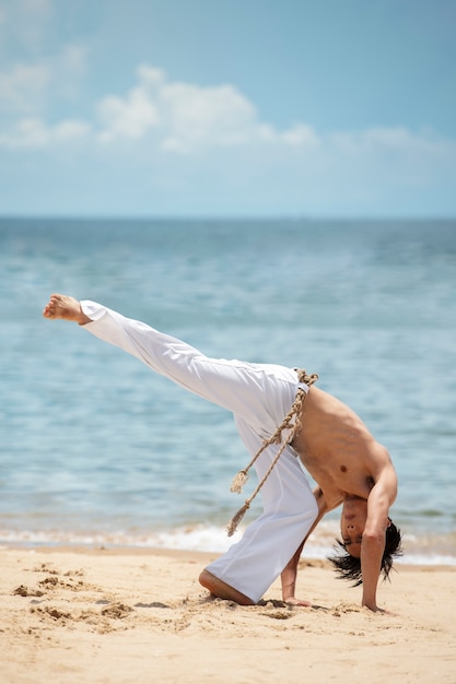 Uomo senza camicia che pratica capoeira da solo sulla spiaggia