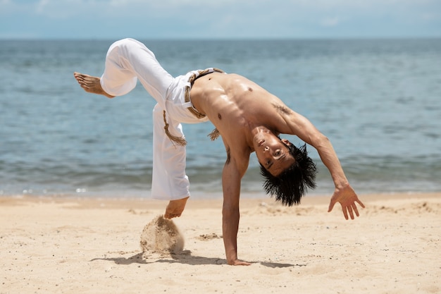 Shirtless man practicing capoeira by himself on the beach