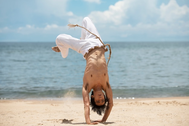 Foto gratuita uomo senza camicia che pratica capoeira da solo sulla spiaggia