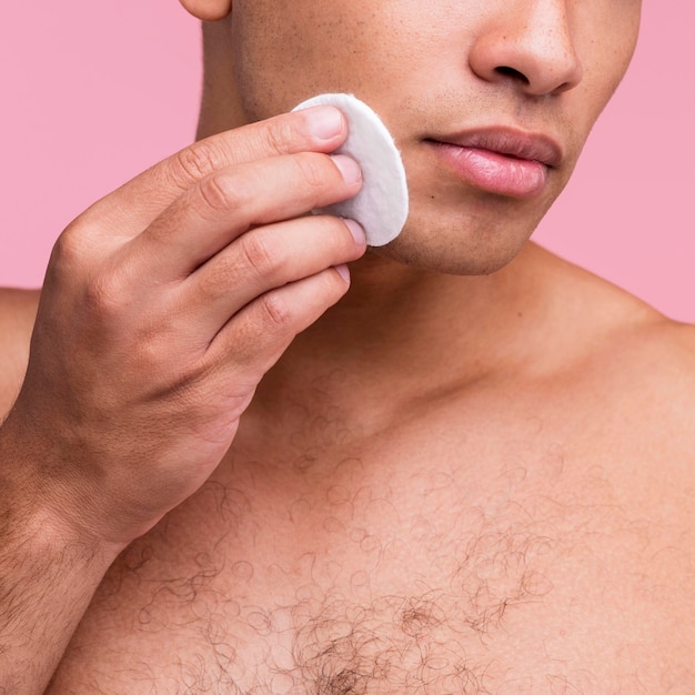 Shirtless man using cotton pads on his face