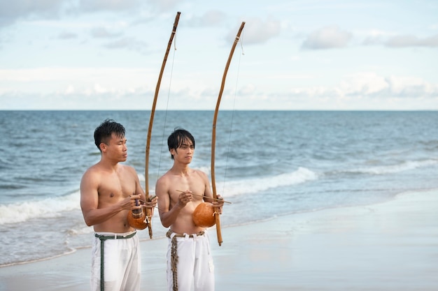 Foto gratuita uomini senza camicia che praticano la capoeira sulla spiaggia con archi di legno