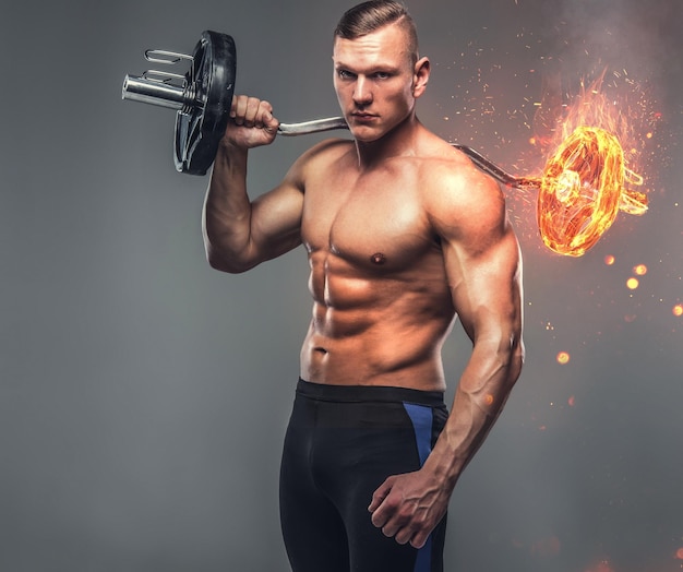 上半身裸の筋肉質の運動男性は、灰色の背景に燃えるバーベルを保持しています。