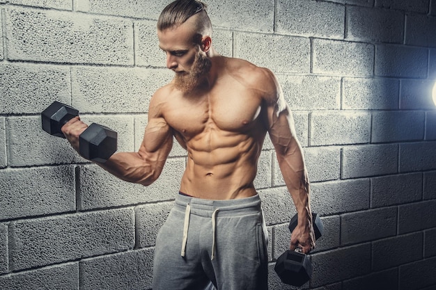 Shirtless muscular bearded man doing exercises with dumbells.