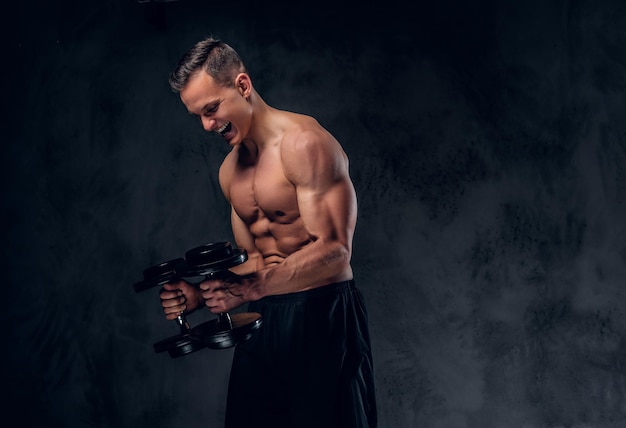 Free photo the shirtless muscular male holds a set of dumbbells over dark grey vignette background.