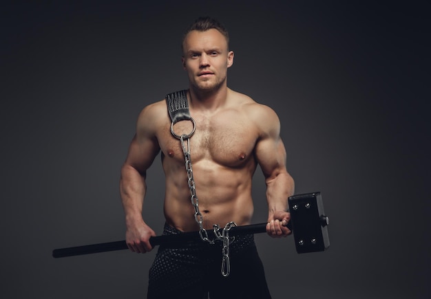 黒のショートパンツで上半身裸の筋肉質の男は、クロスフィットハマーを保持しています。