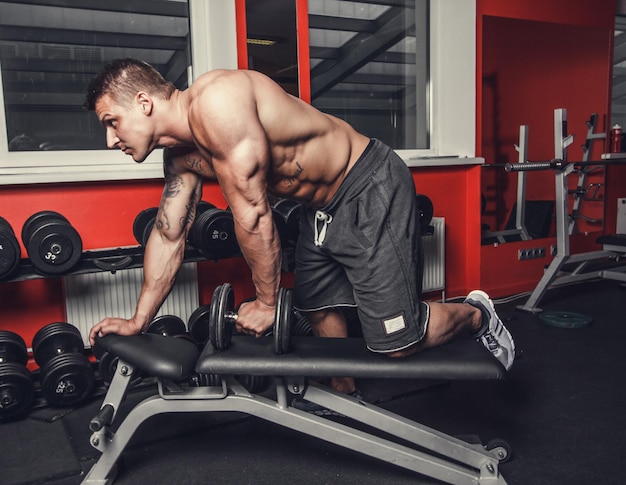 Shirtless muscular man doing triceps workouts in a gym club.