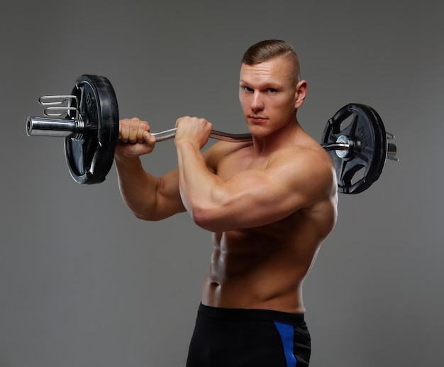 Shirtless muscular man holds barbell. Isolated on a grey background.