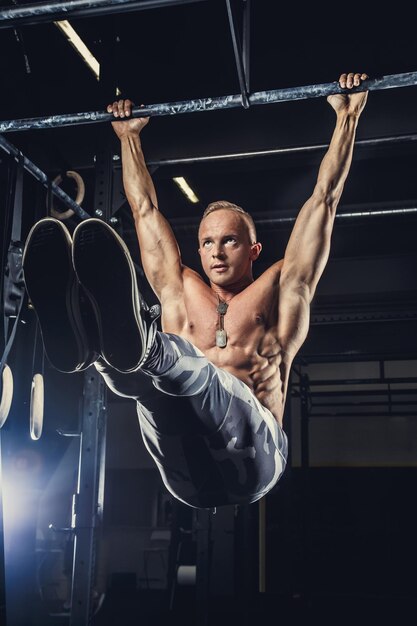 Shirtless muscular man in military pants doing exercises on horizontal bar.