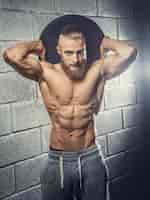 Free photo shirtless muscular man with beard holding disk weight behind his head. grey wall from bricks background.