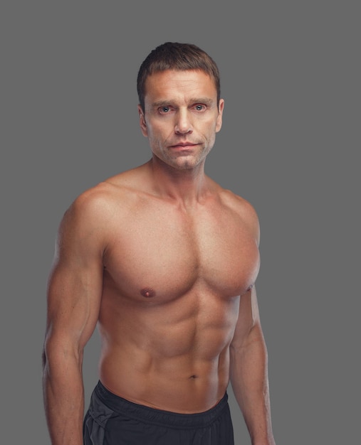Shirtless muscular suntanned middle age male isolated on grey background.